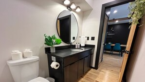 Ein modernes Badezimmer mit Toilette, Waschbecken und Spiegel. Auf dem Waschbecken steht eine Pflanze und ein Handtuch hängt an der Wand.