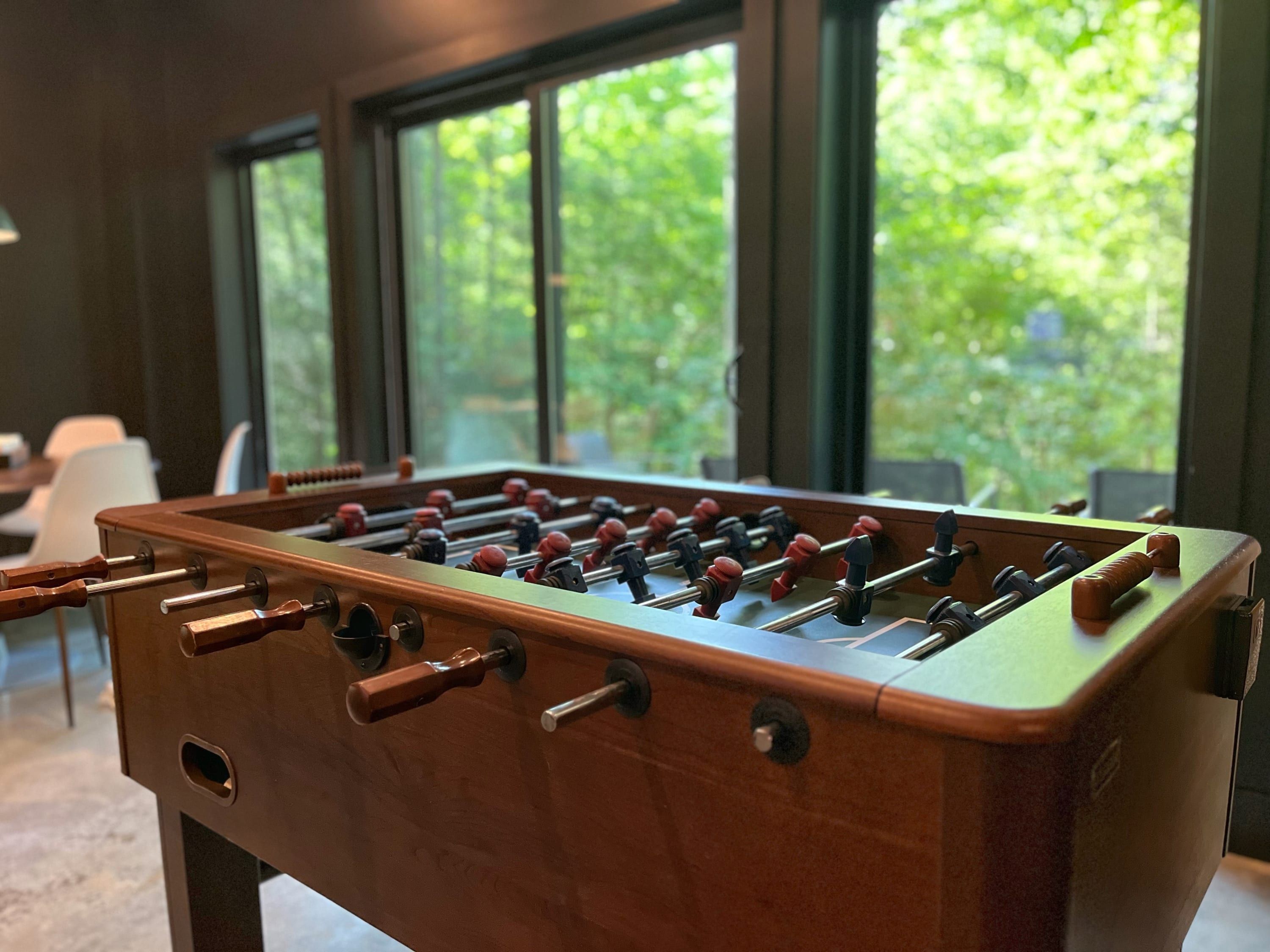 A foosball table in a room with large windows and a view of greenery outside.