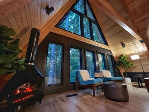 A cozy cabin interior with a fireplace, large windows, and wooden floors. - Two Pines Hollow | Private A-Frame | Hot Tub (Rogers)