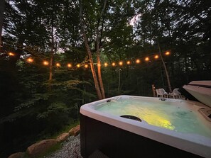 A hot tub surrounded by trees with string lights. - Two Pines Hollow | Private A-Frame | Hot Tub (Rogers)