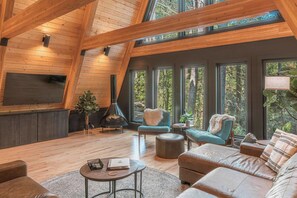 A modern living room with a fireplace, comfortable seating, and large windows offering a view of the outdoors. - Two Pines Hollow | Private A-Frame | Hot Tub (Rogers)