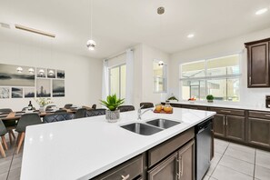 A modern kitchen with a large island, double sink, and dining area with chairs and a table.