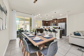 A modern kitchen with dark wood cabinets, stainless steel appliances, and a dining area with a long table and chairs. - 4BR family home - themed rooms & private pool (Kissimmee)