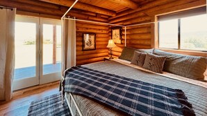 Een slaapkamer in een blokhut met een bed, nachtkastje, lamp en raam.