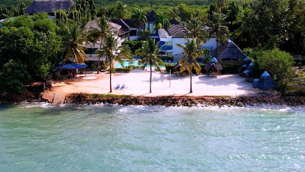 Ein Strandresort mit Pool, Palmen und strohgedeckten Hütten.