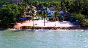 Un resort sulla spiaggia con piscina, palme e capanne con tetto di paglia.