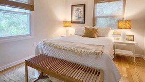 A bedroom with a large bed, two bedside lamps, a wooden bench, and a framed artwork on the wall.