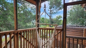 A wooden deck with a hammock hanging from a metal frame, surrounded by trees.