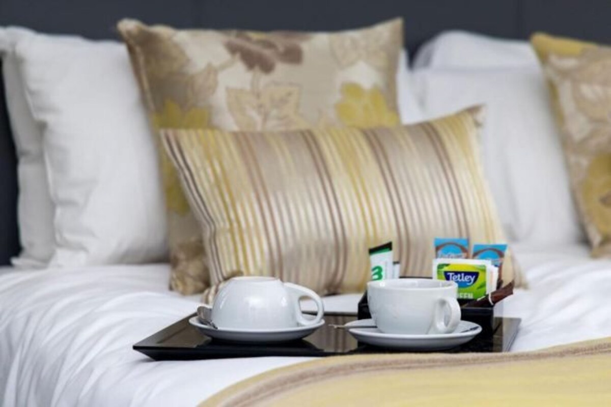 Una cama bien hecha con ropa blanca y una bandeja con una taza y una caja de té Talley.