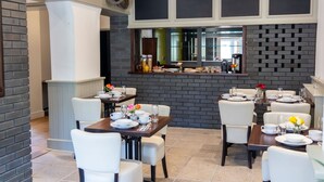 A modern dining area with brick walls, white furniture, and a central island with a coffee machine. - The Bat and Ball (Canterbury)