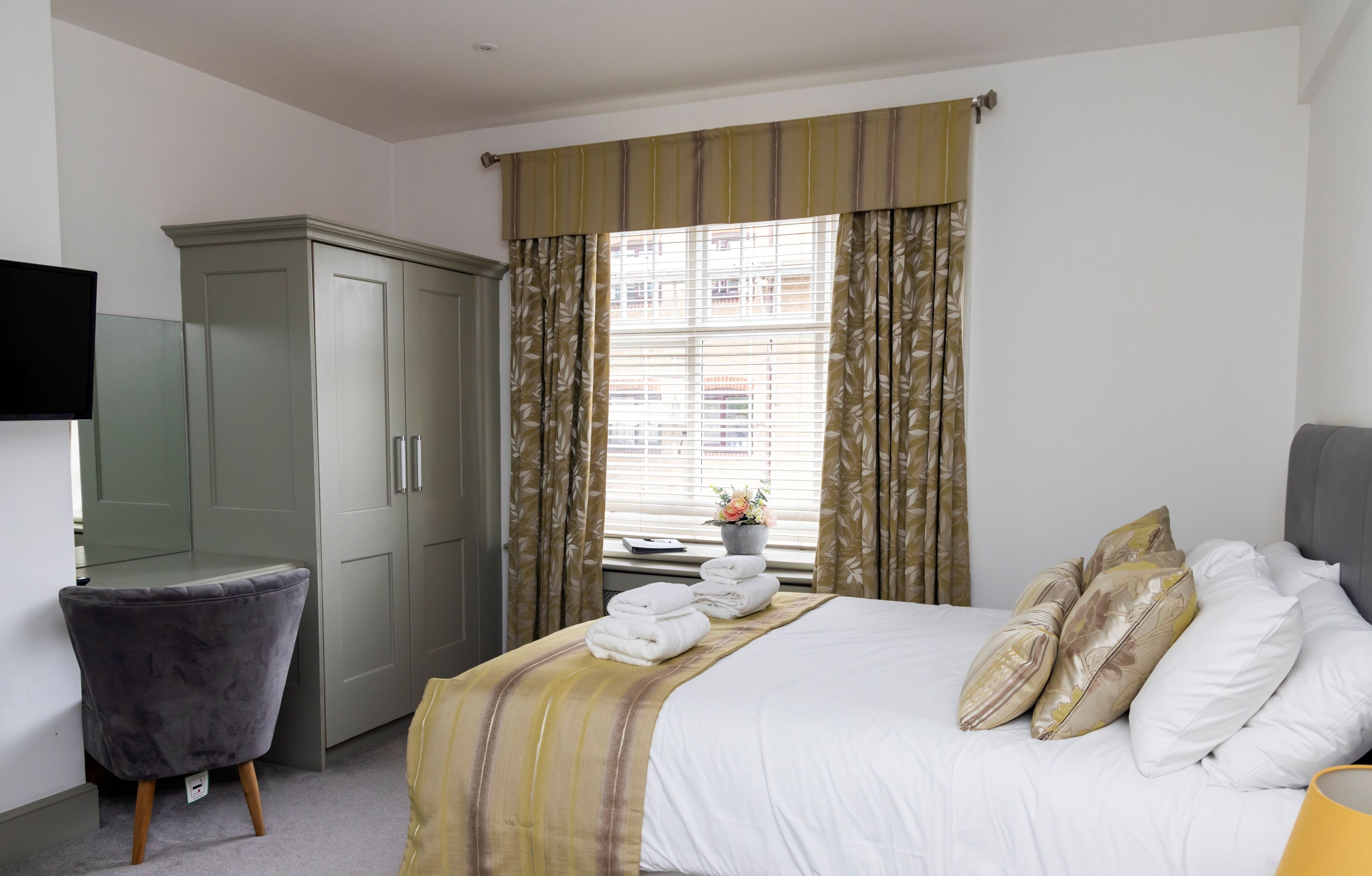 A hotel room with a bed, a wardrobe, a desk, and a window with curtains.