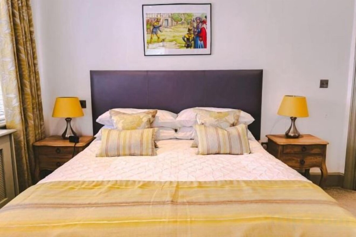 A neatly made bed with pillows and a blanket, two bedside tables with lamps, and a framed picture on the wall.