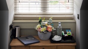 A small, well-lit room with a window, a desk with a laptop, a vase of flowers, and a water bottle. - The Bat and Ball (Canterbury)