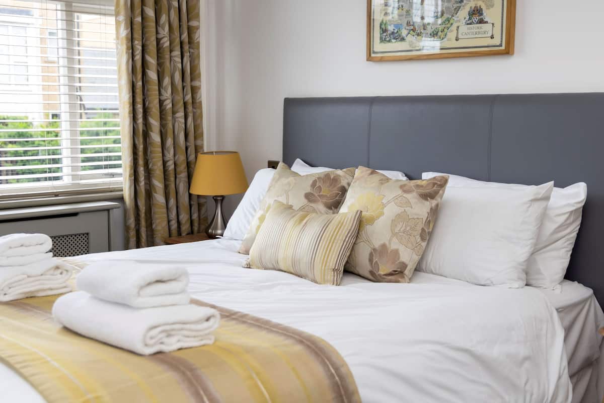 A neatly made bed with white linens and floral-patterned pillows, a lamp, and a framed map on the wall.