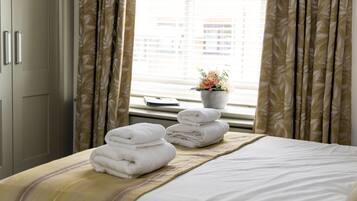A hotel room with a bed, towels, a window with curtains, and a potted plant.