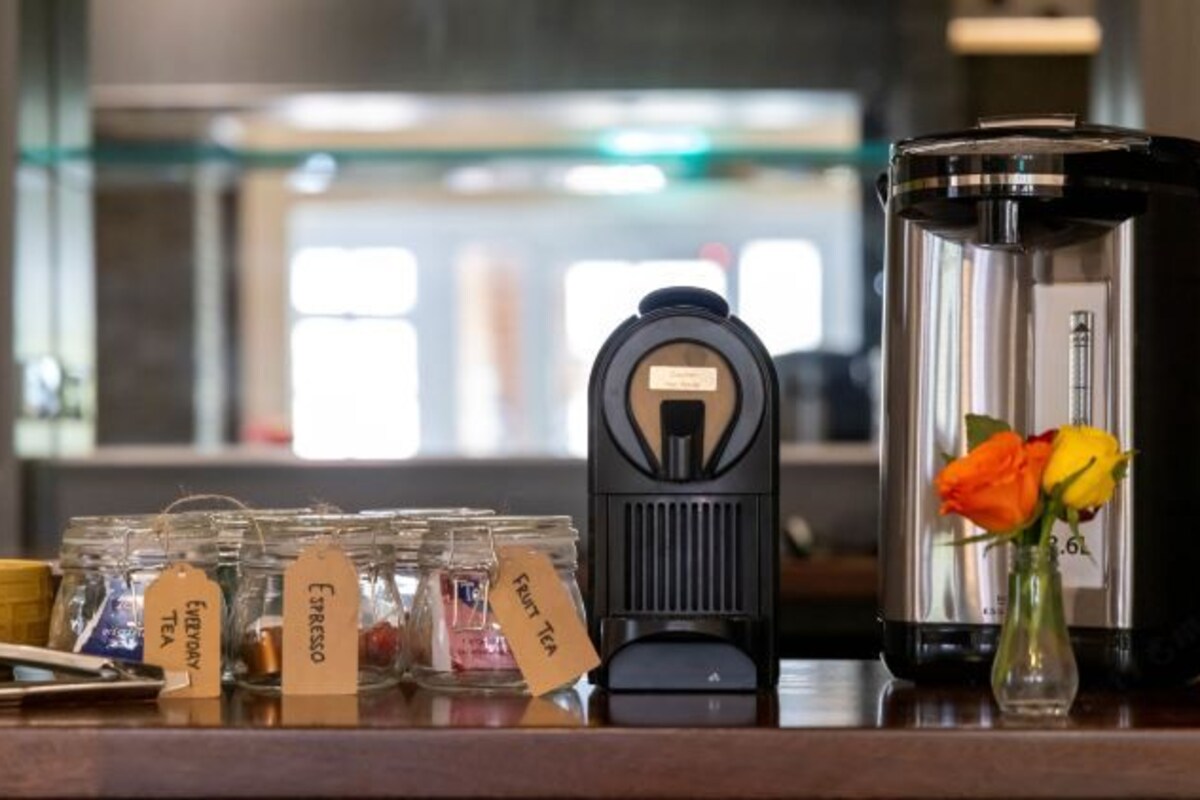 A coffee machine, a large water dispenser, and several labeled jars of tea and fruit tea on a countertop.