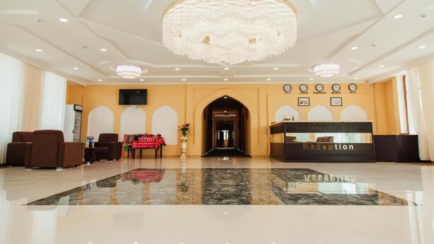 Zona de recepción de hotel con candelabro, mostrador de recepción, área de descanso y piso de mármol pulido.