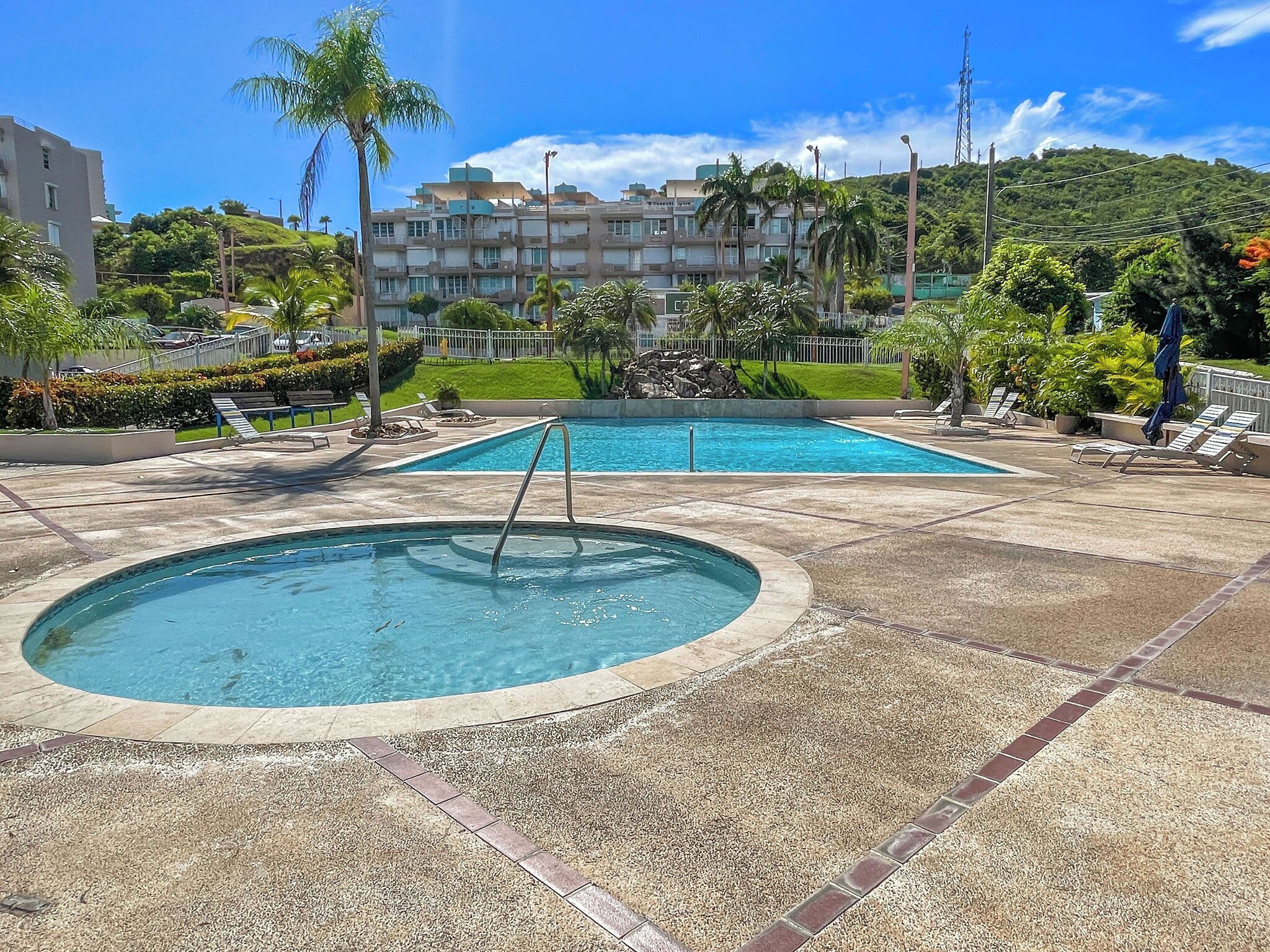A pool area with two pools, one circular and one rectangular, surrounded by lounge chairs and palm trees.