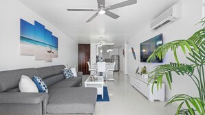 A modern living room with a grey sofa, a coffee table, and a TV. There is a ceiling fan, an air conditioning unit, and a plant. - Perla del Mar | Perfect Beach Escape (Maunabo)