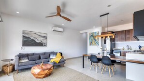 Un salon moderne avec un canapé gris, une table basse en bois et un coin repas avec des chaises noires.