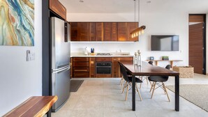 Une cuisine moderne avec des meubles en bois, un réfrigérateur en acier inoxydable et un coin repas comprenant une table et des chaises en bois.