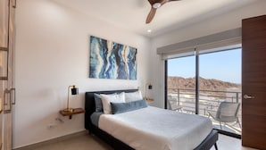 Une chambre moderne avec un grand lit, un ventilateur de plafond, un tableau et un balcon avec vue.