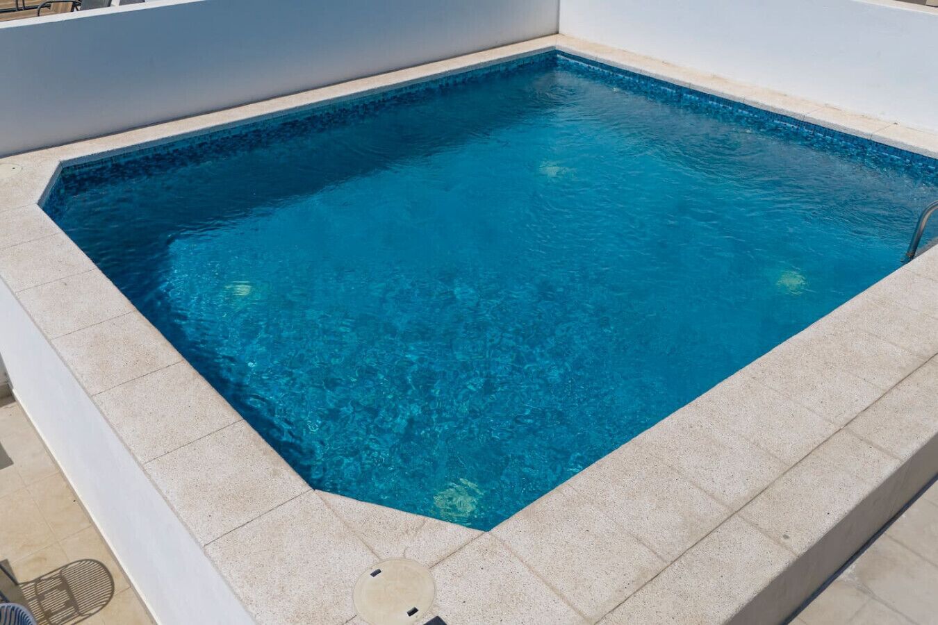 Ein rechteckiger Pool mit klarem, blauem Wasser, umgeben von einer hellen, gefliesten Terrasse.