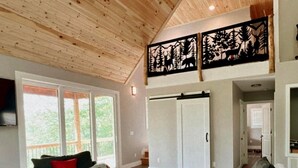 Un salon spacieux avec un plafond haut, une grande fenêtre et une vue sur l’extérieur. On y trouve un canapé avec des coussins rouges, un tapis orné d’un motif d’ours et un placard à portes coulissantes.