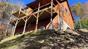 Un grand bâtiment en bois, doté de nombreuses fenêtres et d’un balcon, situé sur une colline au terrain rocheux et à la végétation clairsemée.