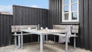 Ein kleiner Sitzbereich im Freien mit einem Metalltisch, Bänken, einem Fenster und einem Holenzaun.