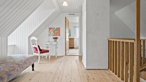Ein geräumiges Schlafzimmer im Dachgeschoss mit schrägen Wänden, einem Holz-Babybett, einem roten Sessel und einem Bett mit gemustertem Bezug.