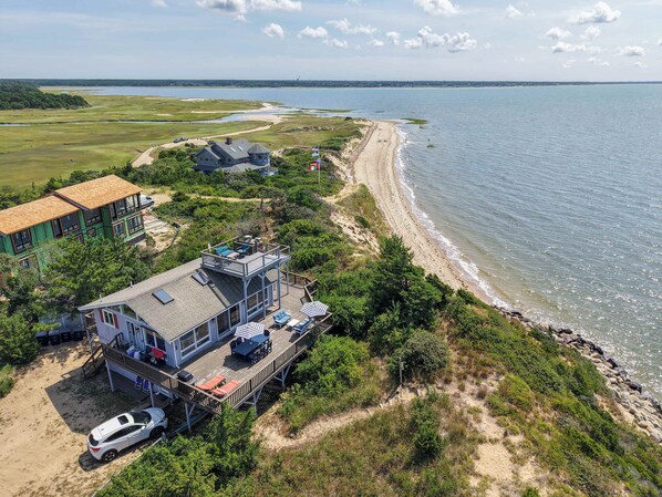A coastal property with a large deck, multiple buildings, and a beach view. - Hot Tub, Waterfront Home with Stunning Views! (Wellfleet)