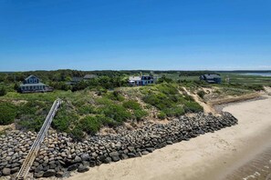 Une zone côtière dotée d’une promenade en bois menant à une plage, entourée de maisons et de végétation.