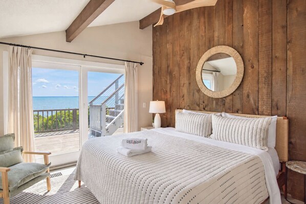 Een hotelkamer met een bed, een ronde spiegel, een nachtkastje, een stoel en uitzicht op de oceaan.