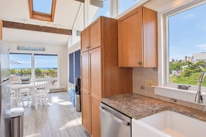 A modern kitchen with wooden cabinets, a granite countertop, and a view of the ocean. - Hot Tub, Waterfront Home with Stunning Views! (Wellfleet)