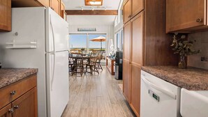 Una cucina con armadietti in legno, un frigorifero bianco, un'area pranzo con tavolo e sedie, e una vista panoramica attraverso ampie finestre.