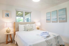A bedroom with a bed, two bedside lamps, a window, and three framed pictures on the wall. - Hot Tub, Waterfront Home with Stunning Views! (Wellfleet)