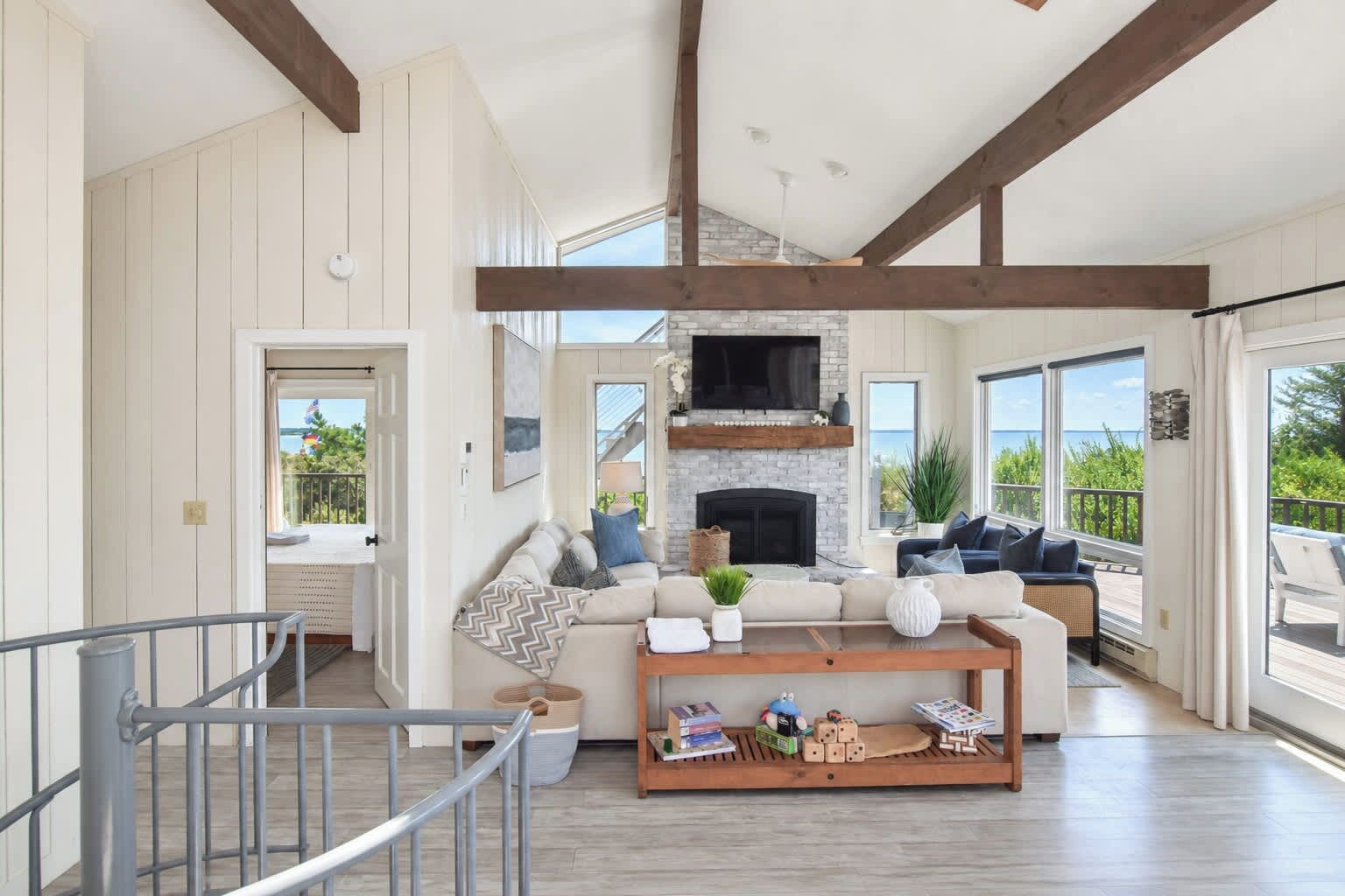 A spacious living room with a fireplace, large windows, and a wooden ceiling.