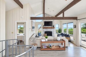 A spacious living room with a fireplace, large windows, and a wooden ceiling. - Hot Tub, Waterfront Home with Stunning Views! (Wellfleet)