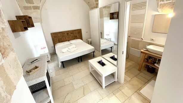 Een moderne hotelkamer met een plafond van natuursteen, een houten bed, een witte nachtkastje, een klein nachtkastje met spiegel, een witte wastafel en een houten kast.