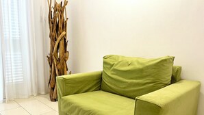 Een groene bank in een kamer met witte muren en een groot houten sculptuur.