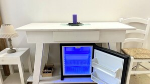 Een witte tafel met een inbouwminibar eronder, een klein houten doosje en een geruit lampje op een bijzettafeltje.