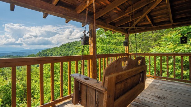 Une terrasse en bois avec un banc et des lanternes suspendues, offrant une vue sur un paysage verdoyant et luxuriant.