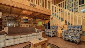LâintĂ©rieur dâun chalet accueillant, avec un escalier en bois, un canapĂ©, des fauteuils Ă motifs, une petite table et un coin cuisine.