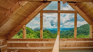 Une piĂšce mansardĂ©e en bois, dotĂ©e dâune grande fenĂȘtre qui offre une vue sur un paysage boisĂ©.