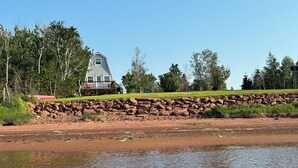 A house with a stone retaining wall and a grassy area in front. - Unplug and relax in this quiet retreat on the shores of Tracadie Bay (Donaldston)