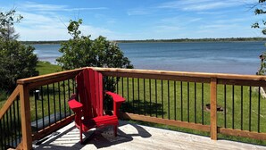 A wooden deck with a red Adirondack chair overlooking a lake. - Unplug and relax in this quiet retreat on the shores of Tracadie Bay (Donaldston)