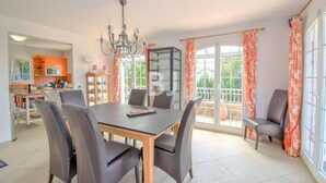 Ein geräumiger Essbereich mit großem Tisch und Stühlen, einer Kandelaber und Blick auf den Garten durch die Schiebeglastüren.
