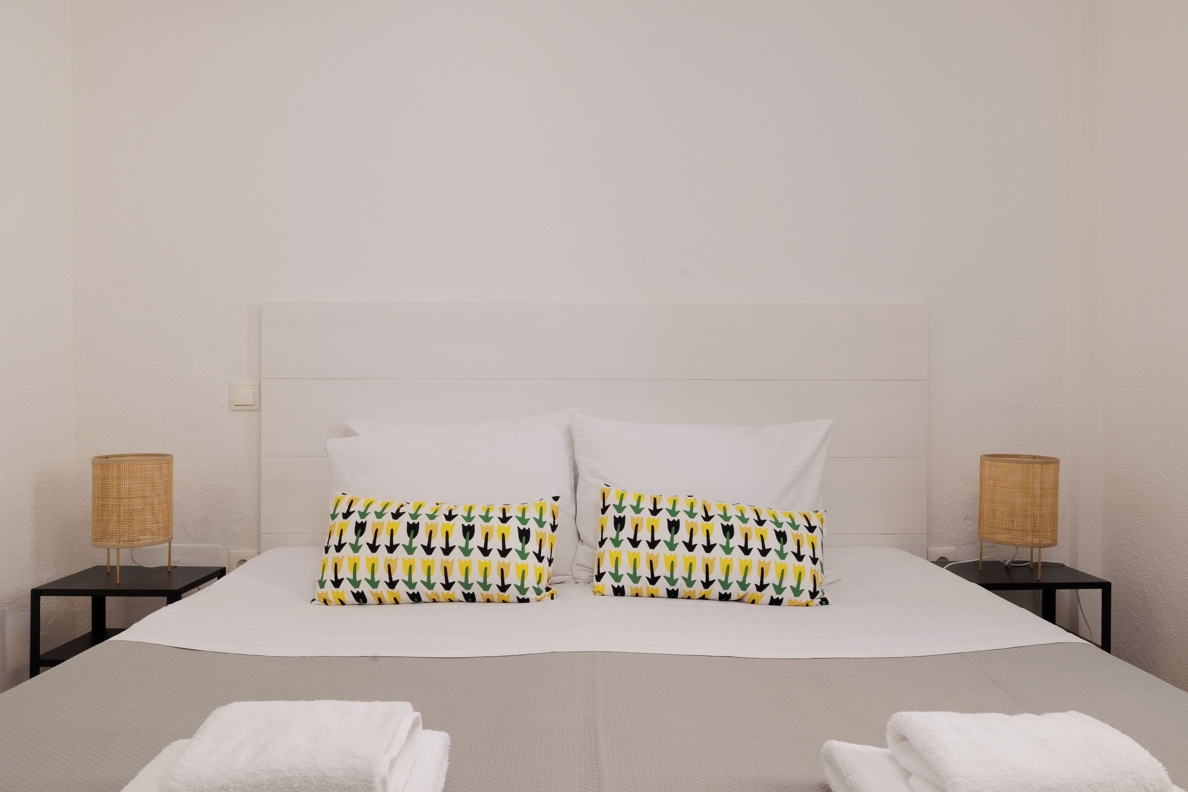 A neatly made bed with white linens, two patterned pillows, and two small bedside tables with lamps.