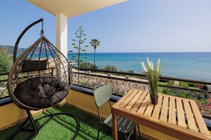 A balcony with a hanging chair, a table, and a potted plant. - Coastal Bliss Apartments (Corfu)